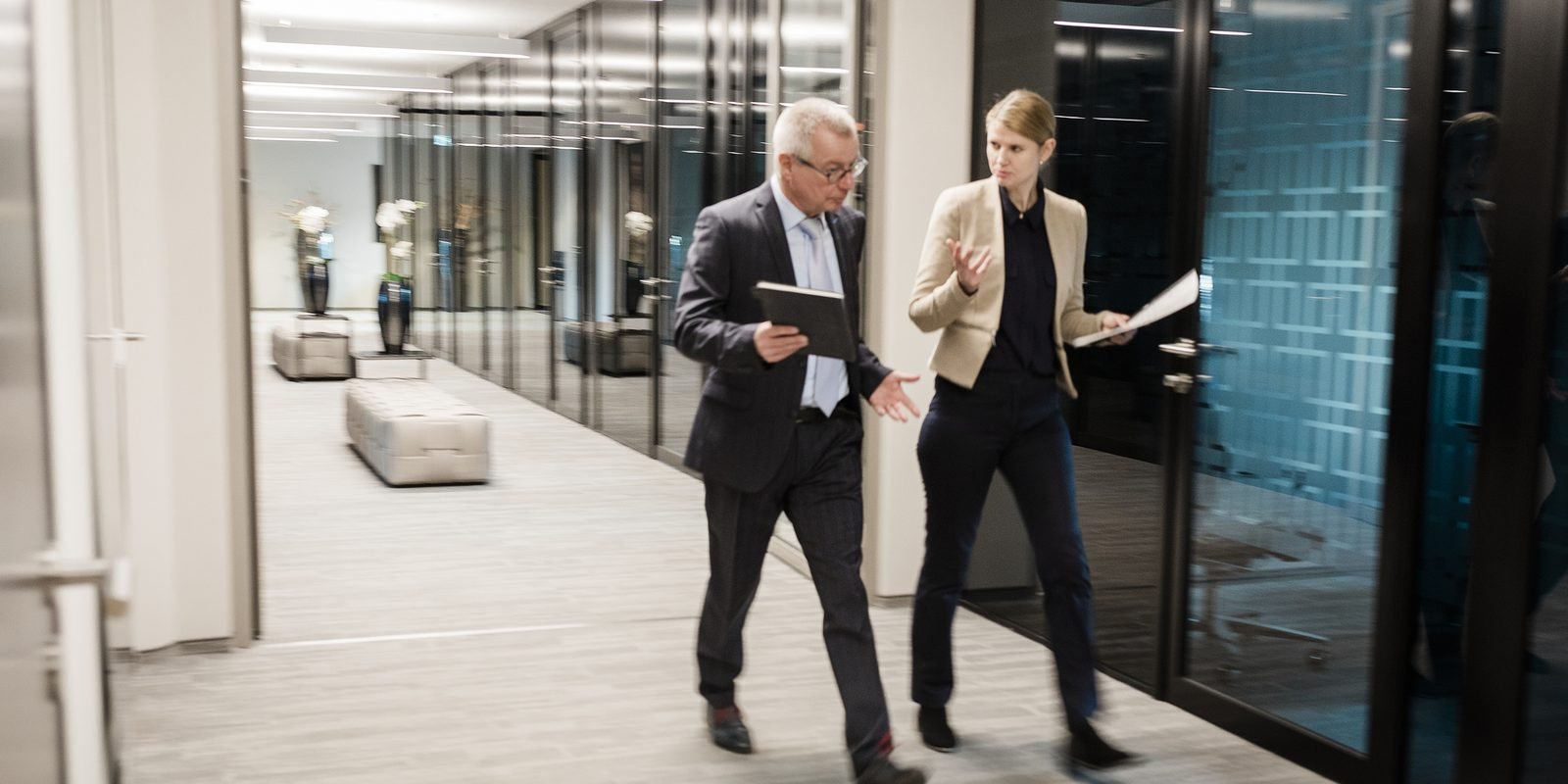 Two colleagues walking and talking in an office corridor